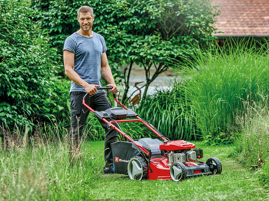 A man stands behind an Einhell petrol lawnmower with automatic battery start.
