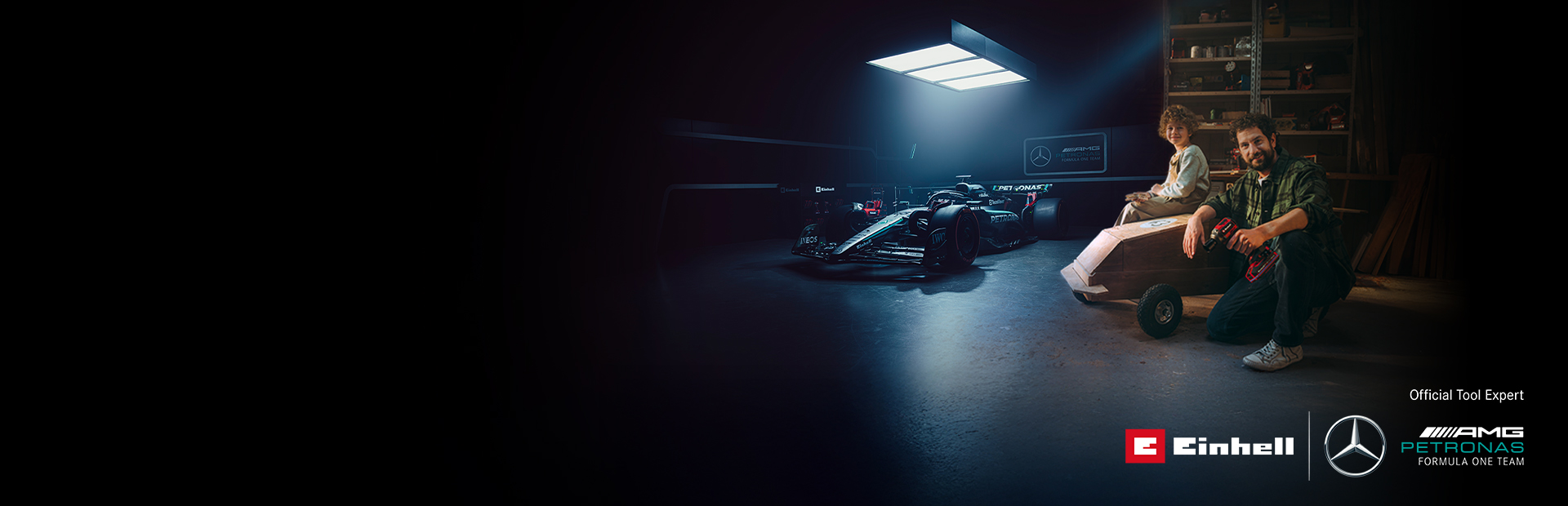 Otac i dijete u radionici s doma napravljenim soapbox autom. U pozadini se nalazi Mercedes-AMG PETRONAS Formula 1 bolid i Einhell alati.