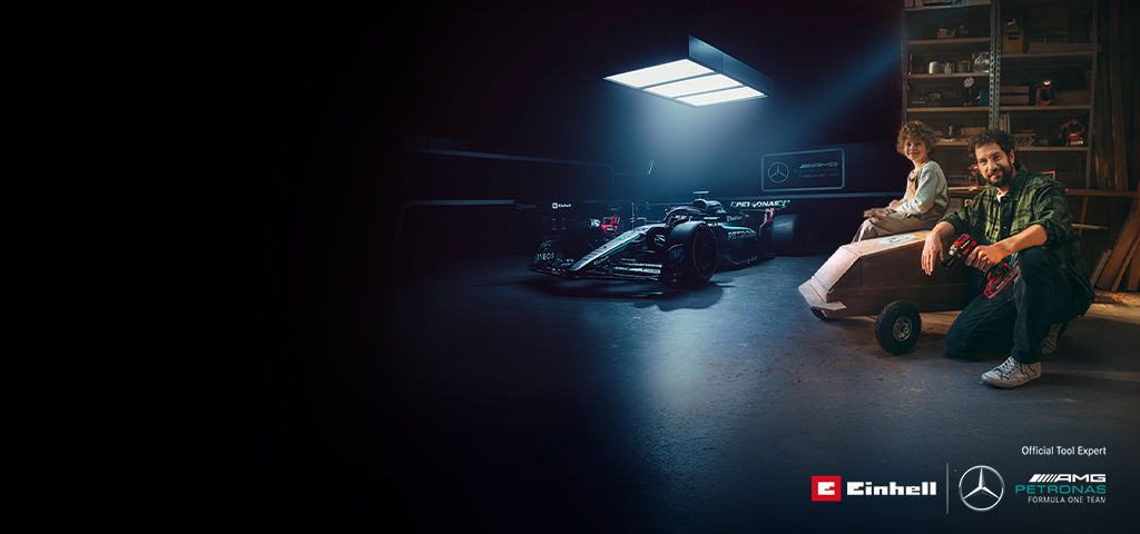 Otac i dijete u radionici s doma napravljenim soapbox autom. U pozadini se nalazi Mercedes-AMG PETRONAS Formula 1 bolid i Einhell alati.